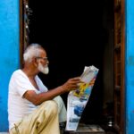 Senior man in white shirt reading a newspaper in a vibrant blue doorway in Bikaner, India.